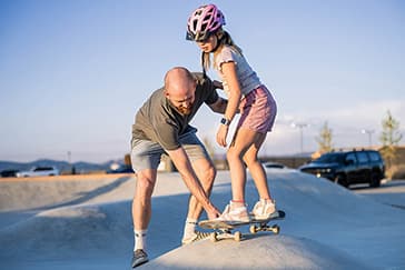 A father teaching his daughter to skateboard at the Firefly wheels park